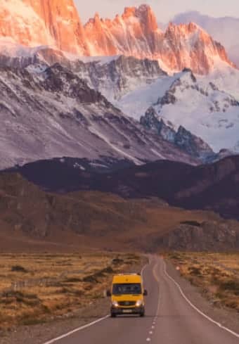 Motorhome amarelo em uma estrada aberta abaixo do maciço Fitz Roy coberto de neve na Patagônia